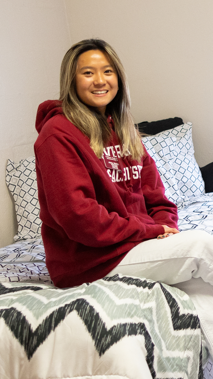 A UMass student sits on her bed in a dorm room.